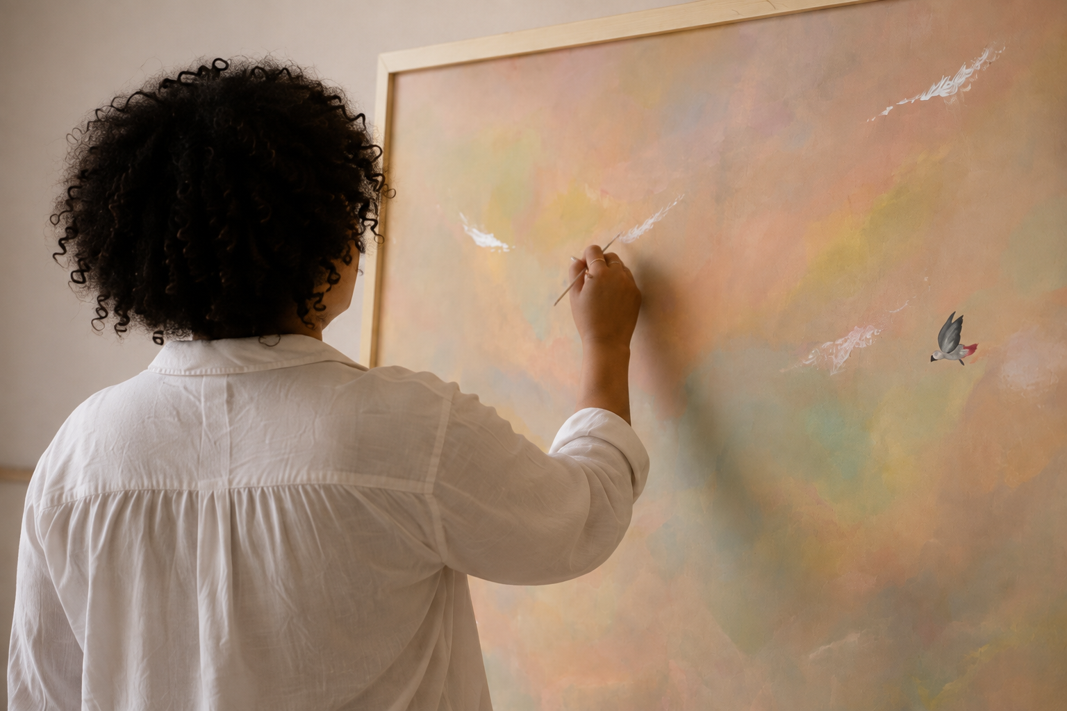 Nolwenn vue de dos, travaillant les détails blancs de son tableau au ciel pastel